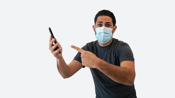 白人男性が白い背景スタジオに隔離された滅菌顔マスクを持つスマートフォンに手を指しています 検疫パンデミックコロナウイルスウイルスの概念で携帯電話のデバイスを示す驚くべき男 — ストック写真