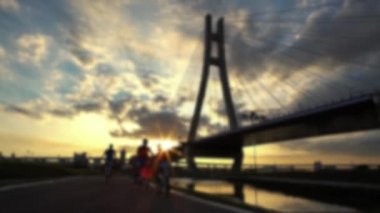 Güneşin batışında New Taipei Köprüsü yolundaki şehir parkında bisiklet süren ve koşan insanların güzel manzarasının odaklanmış görüntüsü. Sağlıklı yaşam için koşu eğitimi.