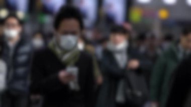 Yavaş çekim ve bulanık odaklanmış Japon iş adamı yüzü maskesi takıyor ve akıllı telefon kullanıyor. Koruyucu Omicron varyant koronavirüs zatürresi olarak maskeyi takan kişi