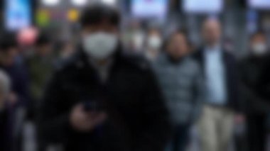 Yavaş çekim ve bulanık görüş. İnternette sörf yapmak için kullanılan telefon cihazını kullanırken cerrahi maske takan insanlar yürüyor. Omicron varyant koronavirüs pnömonisi