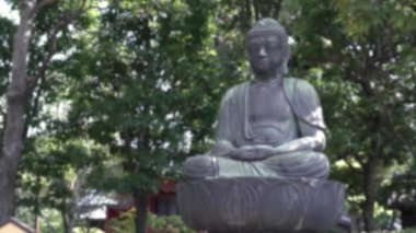 Yeşil çitleri ve ağaçları olan bir Buda heykelinin odaklanmış görüntüsü. Senso-ji 'nin ünlü Budist tapınağında huzurlu bir manzara. Tokyo City, Japonya 'daki Japon tapınağı. Sahnede bulanık arkaplan