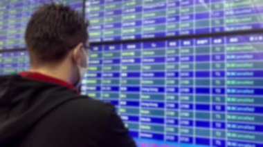 İptal edilmiş uçaklarla havaalanı tahtasına bakan bulanık bir Caurcasian. Toplu taşımada Omicron Covid-19 'un bulaşıcı hastalıklarına karşı koruyucu maske takmak. Coronavirüs