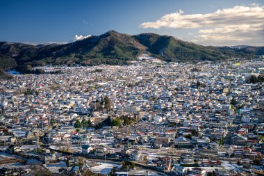 Fujiyoshida Japon şehrinin havadan görünüşü. Ufuktaki dağlarda bitkiler ve binaların etrafındaki parklar var. Japonya 'nın eski kentinin manzarası yükseldi.
