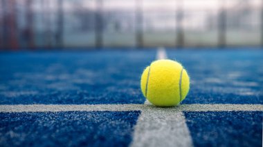 Açık havada mavi kortta kürek ağının arkasında sarı top var. Padel tenisi bir raket oyunudur. Profesyonel spor konsepti