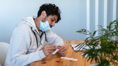 Maske takan bir adam numuneyi evdeki antijen test cihazına yerleştiriyor. Coronavirus 'un enfeksiyonunu kontrol etmek için kaset setini hazırlayın. Karantina salgını.