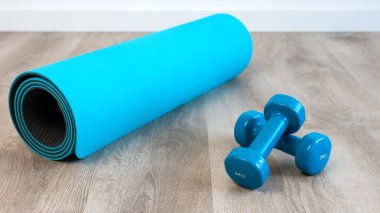 Evde yoga sporu eğitimi için iki mavi dambıl ve hasırla egzersiz yapın. Meditasyon ve spor egzersizleri evde yapılır. Yaşam tarzı ve egzersiz konsepti.