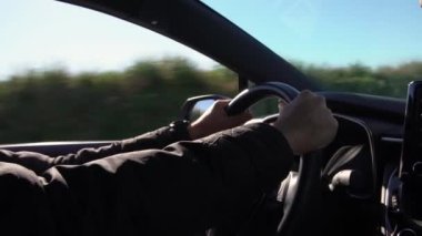 Modern bir yolculukta erkek ellerinin direksiyon simidini tutması. Beyaz bir adam güzel güneşli bir günde otoyolda yeni bir araba kullanıyor..