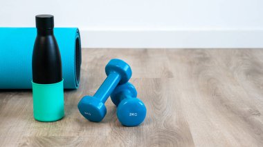 Bir çift mavi dambıl ve evde yerde yoga yapmak için yeniden kullanılabilir metal su şişesi, sabahları sağlıklı meditasyon. Güç eğitimi için spor malzemeleri.