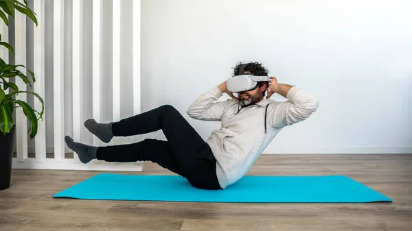 Sportsman enjoying virtual reality glasses to practicing exercise at living room. Man exercising while using vr headset for sport. Smart fitness and innovation concept.