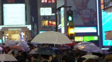Osaka, Japonya-14 Nisan 2019: Geceleyin Dotonbori 'de neon ışıklarıyla yağmurun altında yürüyüş yapan turistlerin yavaşlaması. Yağmurlu bir günde şehirde yürürken şemsiye tutan insanlar
