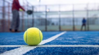 Açık havada mavi kortta kürek ağının arkasında sarı top var. Padel tenis oynayan adam. Beyaz tenli sporcu topa vuruyor. Raket sporu konsepti.