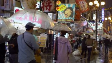 Osaka, Japonya-14 Nisan 2019: Yağmurlu bir günde Dotonbori 'de neon ışıklarıyla yağmurun altında gece alışverişi yapan turistlerin yavaşlaması. Dotombori Bölgesi