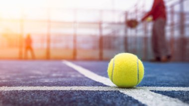 Açık havada mavi kortta kürek ağının arkasında sarı top var. Padel tenis oynayan adam. Beyaz tenli sporcu topa vuruyor. Raket sporu konsepti.