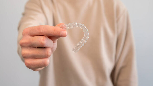 Adult man holds invisalign transparent braces for dental correction. Caucasian person holding invisible orthodontic retainer and aligner. Plastic braces dentistry to straighten teeth in dentist office