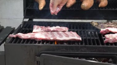 Aşçıbaşı yavaş yavaş ızgarada domuz pirzolası pişirmek için tuz koyuyor. İspanya 'da tatil tatillerinde mangalda pişirilmiş leziz domuz eti..