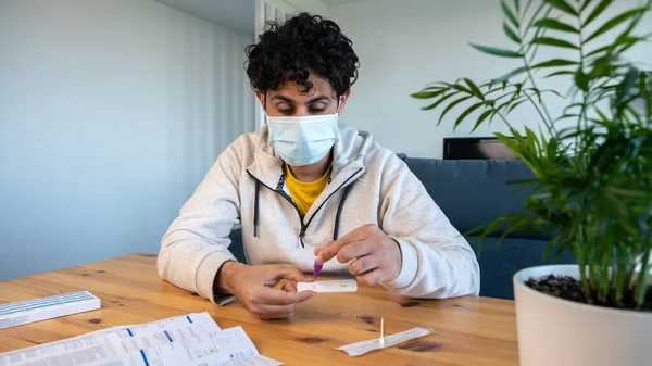 Man wearing mask placing the sample into a buffer dropper for seft detection of coronavirus at home. PCR test after come back from crowd and meeting people. Quarantine pandemic.