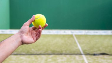 Yeşil tenis kortunda beyaz bir öğrenciye Padel sınıfı öğretmek için elinde raket tenis topu tutan monitör. Erkek oyuncu açık alanda maç yapıyor.