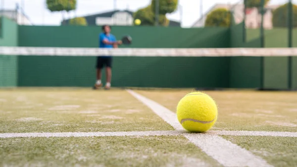 Yellow ball on floor behind paddle net in green court outdoors. Man who playing padel tennis. Caucasian player sportsman hitting balls. Racquet sport game concept.