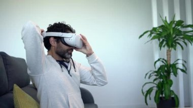 Oturma odasındaki koltukta oturup sanal gerçeklik görüşü izleyen sakallı adam sanal gerçeklik konseptindeki eğlenceli siber deneyimin tadını çıkarıyor.