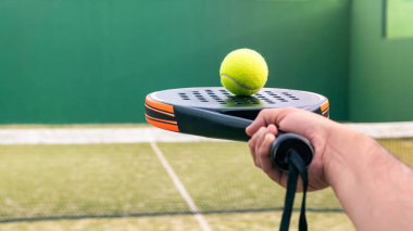 Kafkasyalı bir adam dışarıda yeşil bir kort çimenliğinde topu padel raketinin tepesinde tutuyor. Kürek bir raket oyunudur. Metin için alanı olan profesyonel spor kavramı
