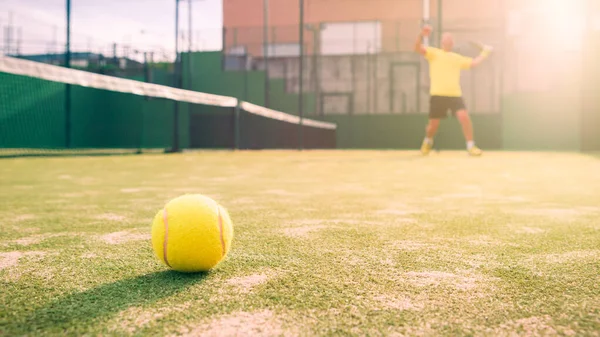 A caucasian padel player jump to the ball, good looking for posts and poster. Man with black racket playing a match in the open behind the net court outdoors. Paddle is a racquet game. Racquet game