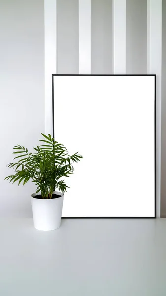 Modern panel with plant in an office room. Minimalist black frame mockup on white background for the design of advertisements. Square frame against a wall.