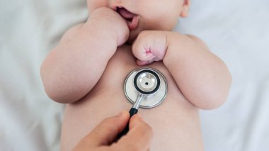 Female doctor examining baby boy toddler listening to lungs with stethoscope. A nurse having medical checkup with sick little newborn patient in clinic. Pediatrician's appointment, healthcare concept