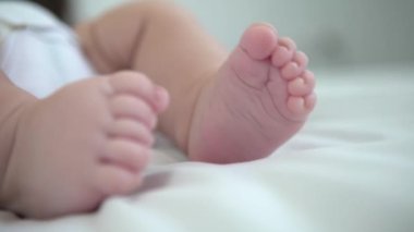 A chubby foot of little baby on white sheet background. Cute newborn age of 3 months. Boy sleeping on the mother's bed. Family maternity concept