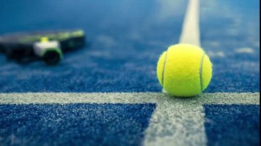 Açık havada mavi kortta kürek ağının arkasında sarı top var. Padel tenisi bir raket oyunudur. Profesyonel spor konsepti