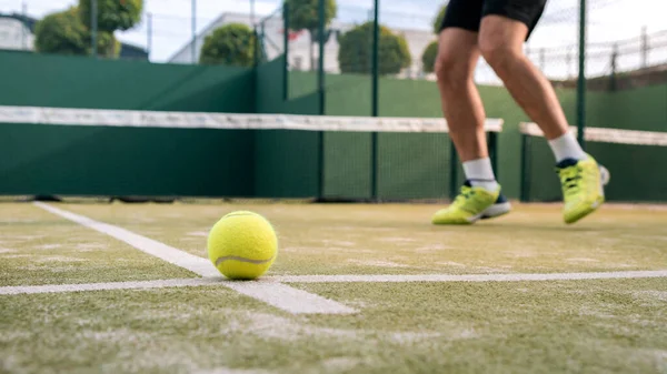 Yellow ball on floor behind paddle net in green court outdoors. Man who playing padel tennis. Caucasian player sportsman hitting balls. Racquet sport game concept.