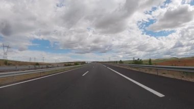 POV driving a car on empty highway road through the fields outside the city during sunny day. Two way asphalt road country views with low clouds at Spain. Traffic ways transportation concept.