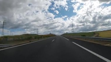 Timelapse of POV driving a car on empty highway road through the fields outside the city during sunny day. Two way asphalt road country views with clouds at Spain. Traffic ways transportation concept.