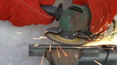 Worker in special clothes and gloves grinding metal with a circular saw in his workshop, bright sparks of metalworking fly in different directions.