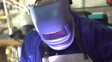 Slowmotion of a man welder with safety helmet working with arc welding machine in the workshop, sideways flashes