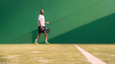 Bir Padel oyuncusu topa atlıyor, iyi görünümlü direkler ve posterler. Siyah raketli bir adam açık alanda, açık alanda, açık alanda maç yapıyor. Metin için alanı olan profesyonel spor kavramı