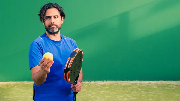 Monitor of padel holding black racket with yellow tennis ball in the hand. Class to student on outdoor tennis court. Man paddel player playing a match in the open