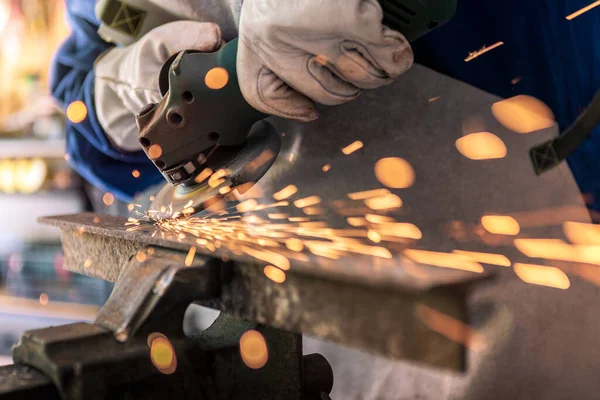 Worker grinding metal with a grinder and cleaning the steel seam. Working in a metal processing workshop. The man works with an electric tool. Sparks from metal heating.