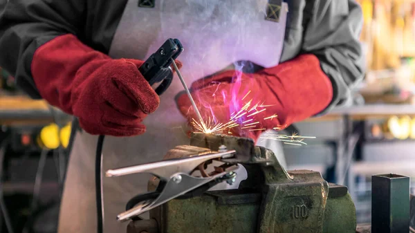 Craftsman working with arc welding machine in workshop. Piece of iron with sparks fly in different directions. Male worker hand welding steel rack.