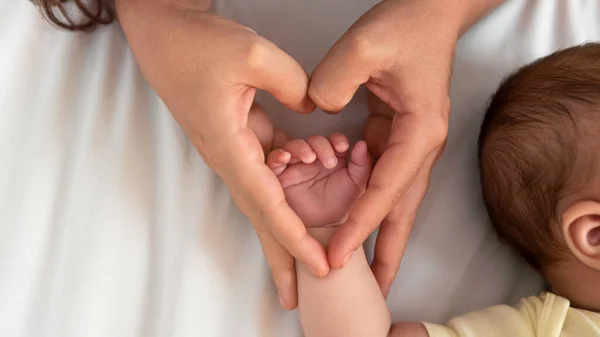 Mom hands holding newborn fingers and giving heart signal. A beautiful conceptual image of motherhood and baby. Love family healthcare and medical body part.