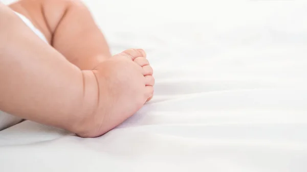 A chubby foot of little baby on white sheet background. Cute newborn age of 3 months. Boy sleeping on the mother\'s bed. Family maternity concept