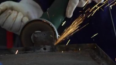 Slowmotion of worker in special clothes and gloves grinding metal with a circular saw in his workshop, bright sparks of metalworking fly in different directions.