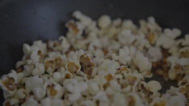 Slowmotion of crunchy popcorn snack. A stainless pan cooking and flying tasty corns grains. Cook delicious and tasty pop corn. Making sweet or salt cinema food commercial.