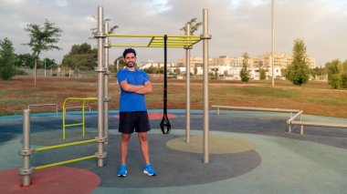 Portrait of confident caucasian man exercising outside in sunny park. Great TRX workout. Young handsome guy in sportswear doing exercising outdoors. Healthy lifestyle concept.