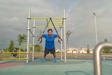 Caucasian man exercising outside in sunny park. Great TRX workout. Young handsome guy in sportswear doing exercising outdoors. Healthy lifestyle concept.