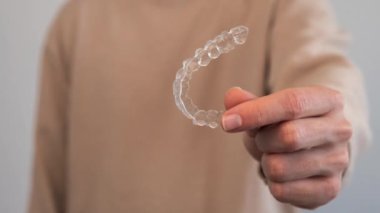 Kafkasyalı genç adam diş düzeltmesi için görünmez silikon hizalayıcı gösteriyor. Dişleri düzeltmek için plastik diş tellerini tutan erkek el.
