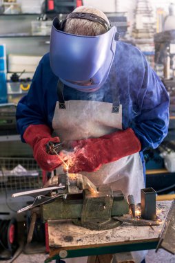 Metal processing with a man using welding machine for steel seam. Locksmith in special clothes, helmet and gloves to works in production. Sparks in metalworking.