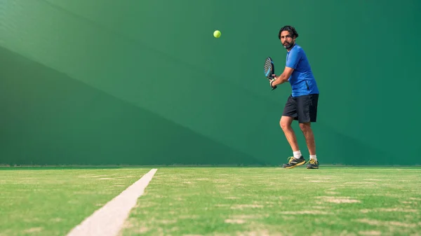 A caucasian padel player jump to the ball, good looking for posts and poster. Man with black racket playing a match in the open behind the net court outdoors. Paddle is a racquet game. Racquet game