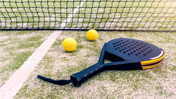 Padel racket and yellow ball behind net on a green court grass turf outdoors. Paddle is a racquet game. Professional sport concept with space for text