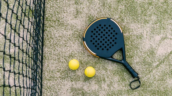 Top view of yellow balls on floor near of padel tennis racket in green court outdoors with natural lighting. Paddle is a racquet game. Professional sport concept