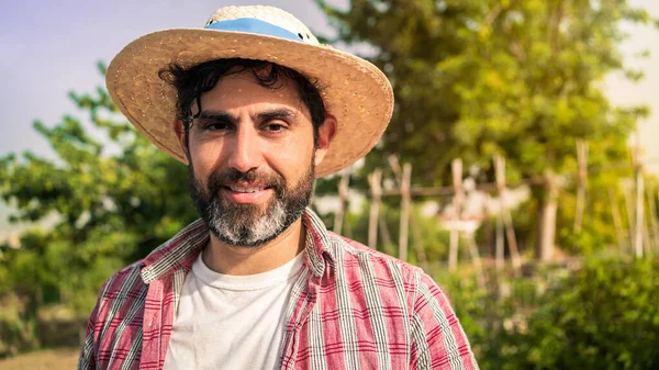 Portrait of a modern bearded farmer man looking at camera smile and stands in the agricultural field. Cheerful male worker in agricultural farm.